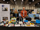 Two Center for Assistive Technology employees standing at a table displaying assistive technologies. 
