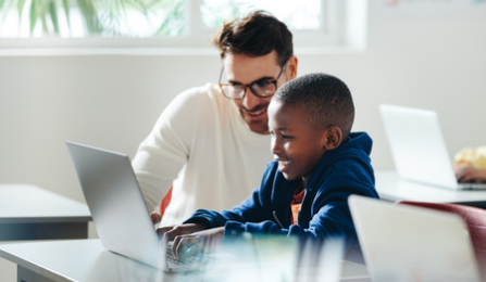 A teacher assists a student with a computer. 