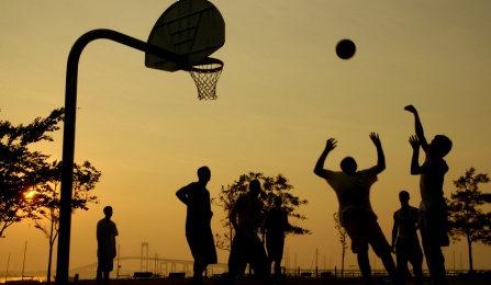 A group of people playing basketball at sunset. 