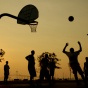 A group of people playing basketball at sunset. 