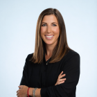 Photo of a dark haired white woman wearing dark clothing against a light gray background. 