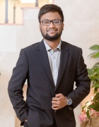 Zoom image: Image of a man in a suit against a cream background with plants to the left side