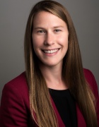 Photo of a woman with long brunette hair from the shoulders up with a red cardigan over a dark shirt. 
