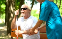A nurse helping a blind man sit on a bench. 