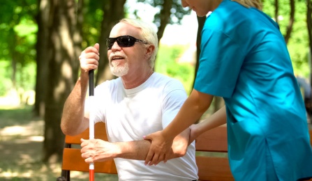 A nurse helping a blind man sit on a bench. 