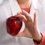 Person in a lab coat holding an apple. 