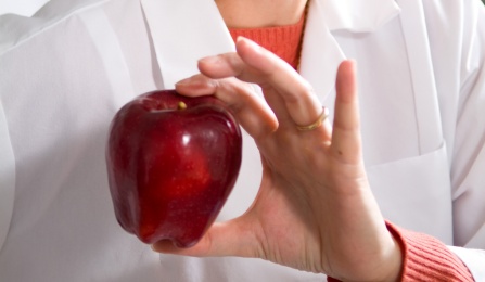 Person in a lab coat holding an apple. 