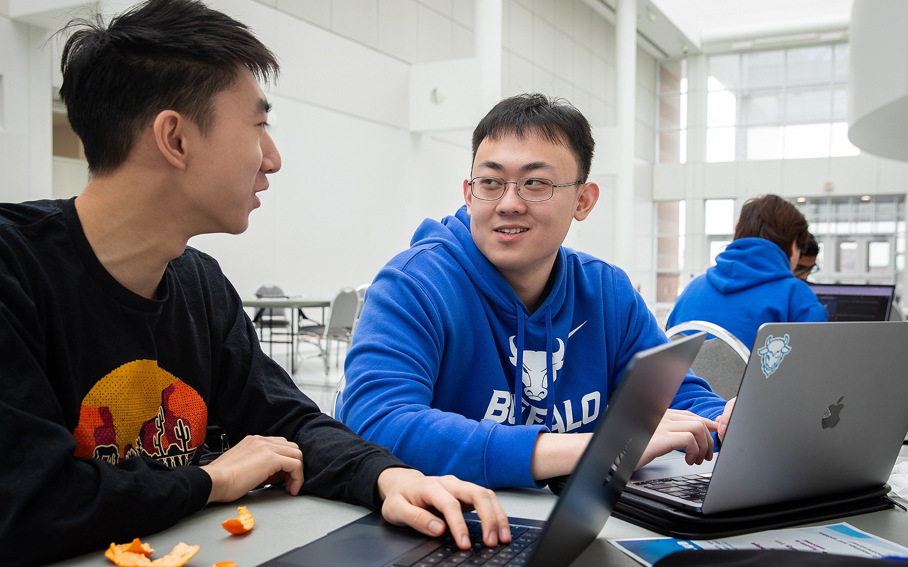 Two people smile at each other as they work on computers. 