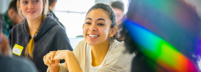 Students discuss a topic while at the University at Buffalo, with a prism effect overlaying the profile of the student in the right-side foreground. 