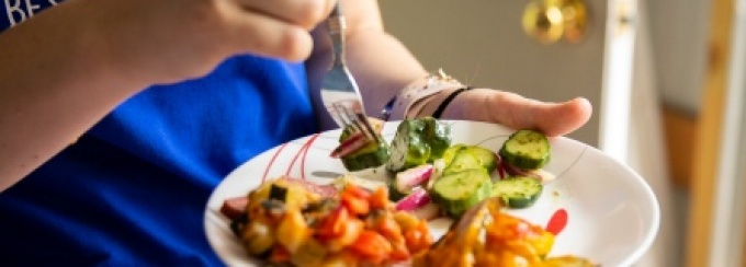 A young adult eats a healthy meal from a white plate with a fork. 