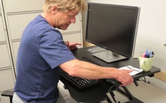 Dr. Lenker adjusts a mechanical sit-stand desk. 