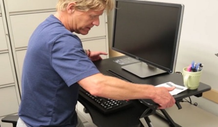 Dr. Lenker adjusts a mechanical sit-stand desk. 