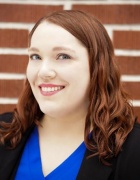 professional headshot photo of Erin Brunelle smiling in front of a brick wall. 