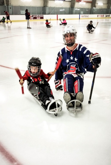 Adult and child on ice hockey sleds. 